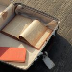 An open vintage suitcase filled with books on a textured pavement, evoking travel nostalgia.